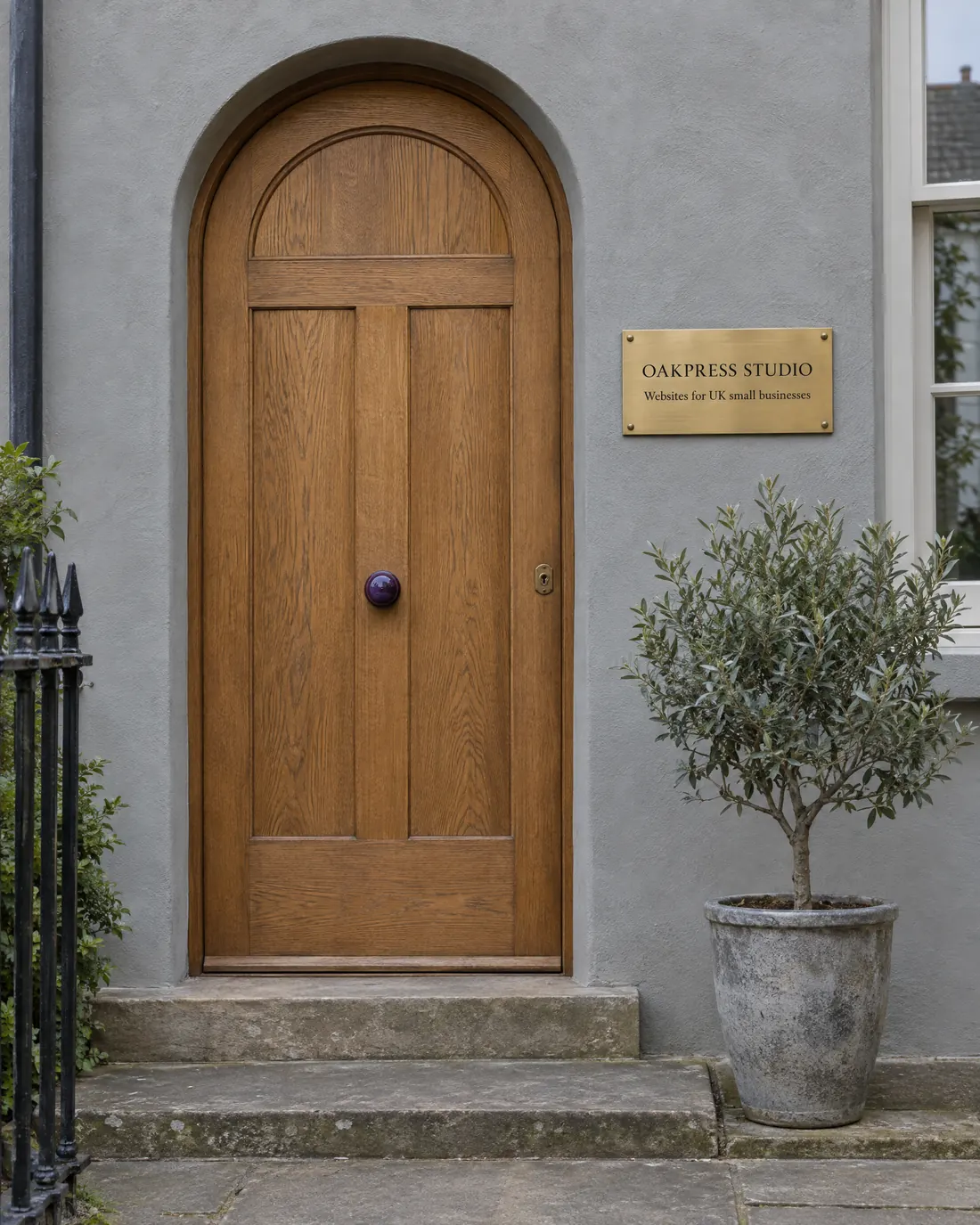 An arched oak front door with a brass Oakpress Studio plaque, set in a lime-plaster wall